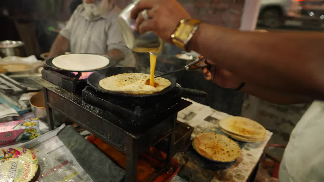 Hand pouring beaten egg into a pocketed paratha on a cast-iron tawa