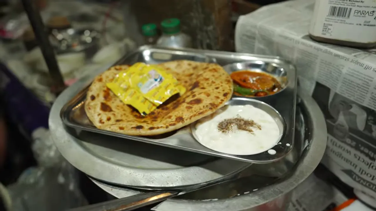 aloo paratha on a stainless-steel tray with a bowl of raita and a bowl of pickle