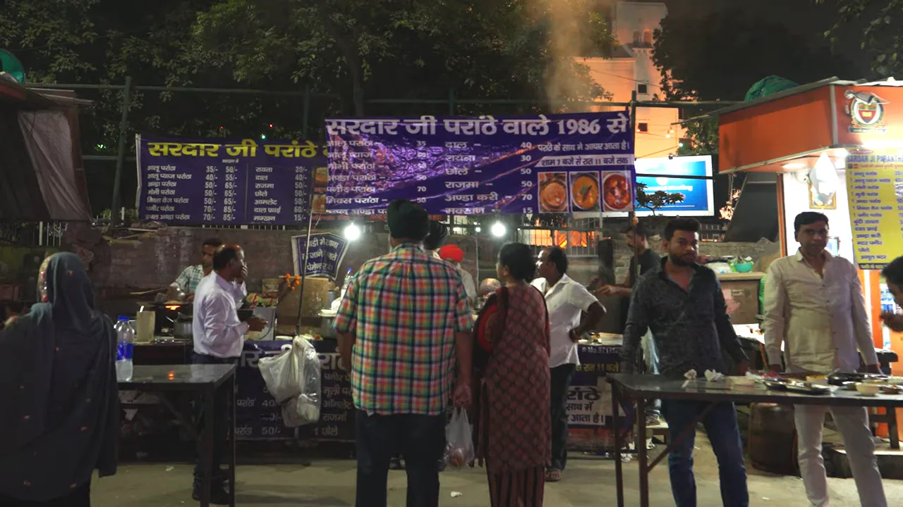 nighttime paratha stall with customers in line and menu board