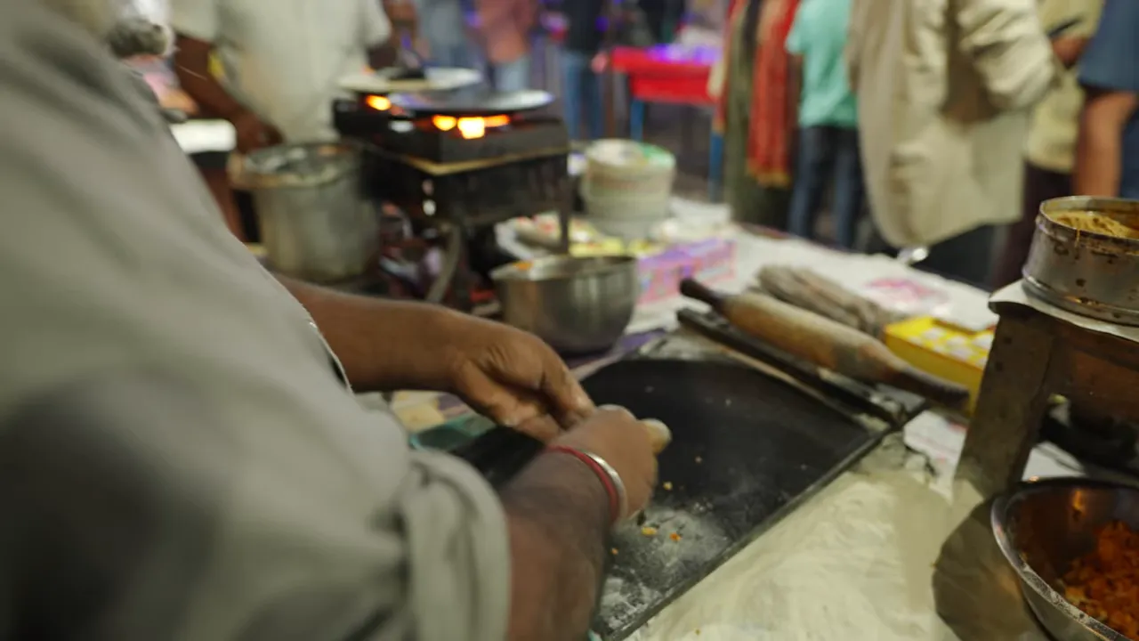 hands shaping a stuffed paratha beside a hot tawa with rolling pins and spice bowls