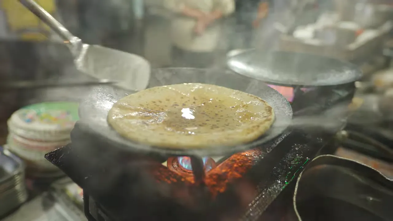 paratha puffing on a hot tawa with steam rising while ghee is brushed on, street-stall setting