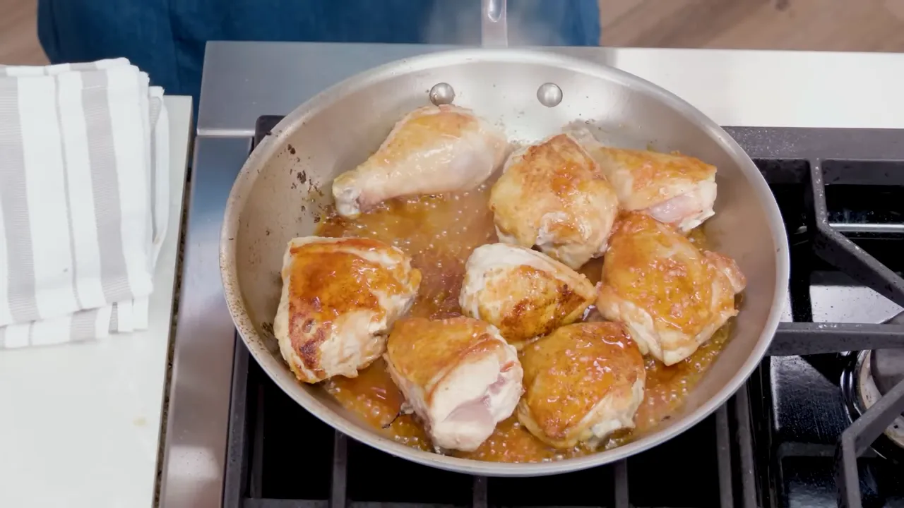 Skillet of browned chicken pieces resting in a glossy hot honey pan sauce