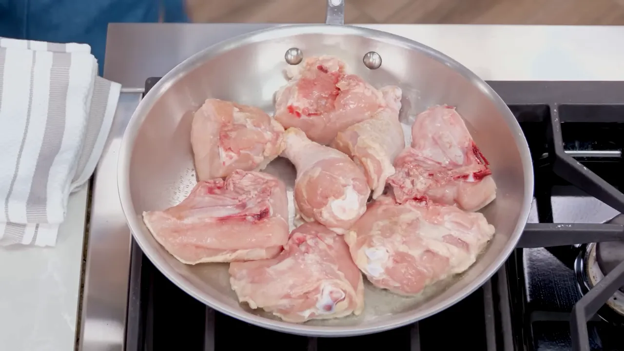 Raw chicken pieces in a stainless skillet ready to be browned