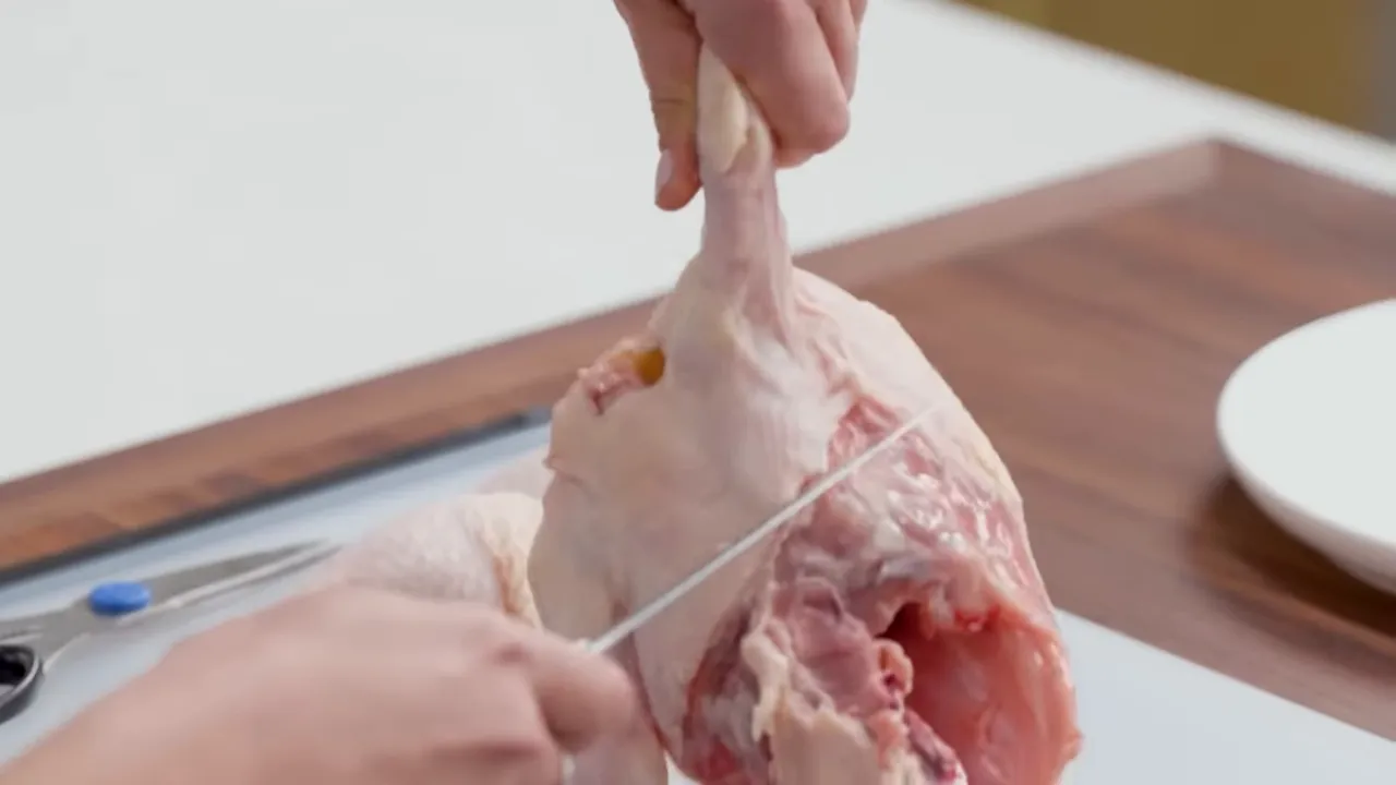 Hands cutting out the backbone of a raw chicken on a cutting board to break it down