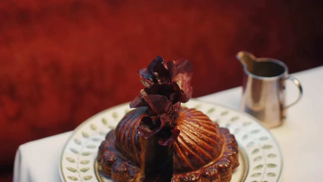 Plated pithiviers with a deep golden, glossy crust on a decorative plate next to a sauce pitcher