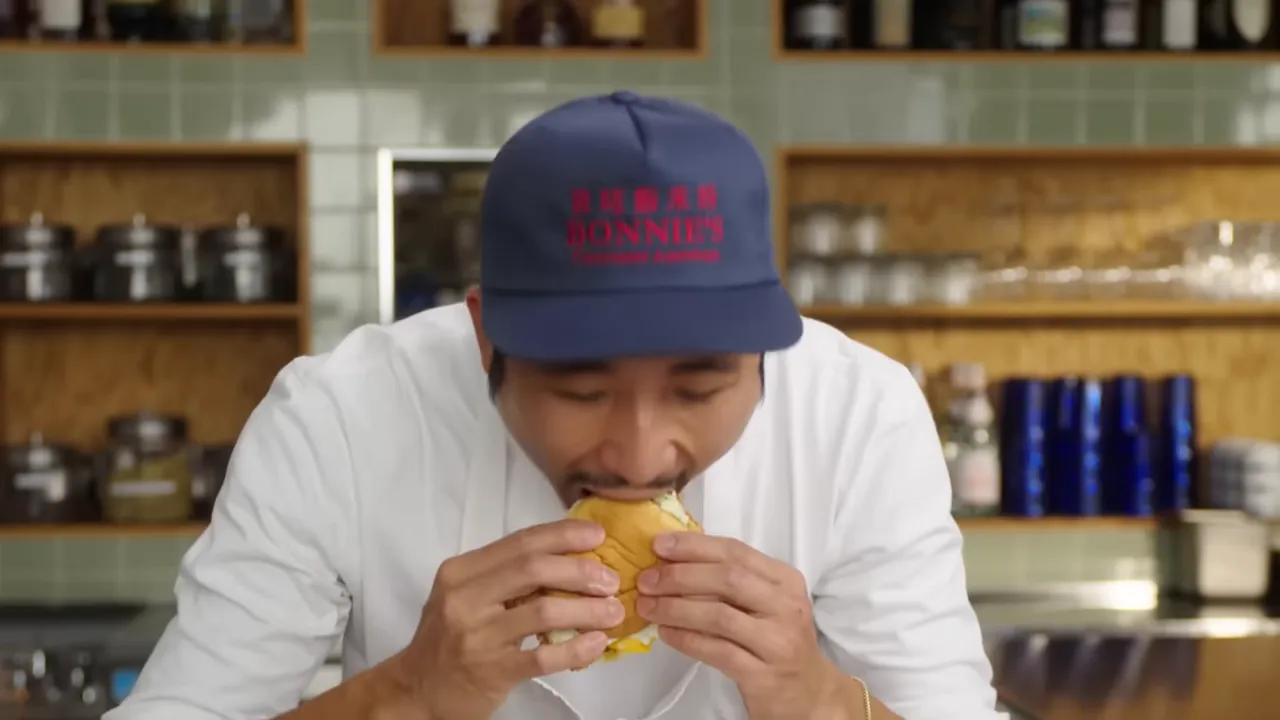 person taking a bite of a Cantonese-style fish sandwich with potato roll and cheese