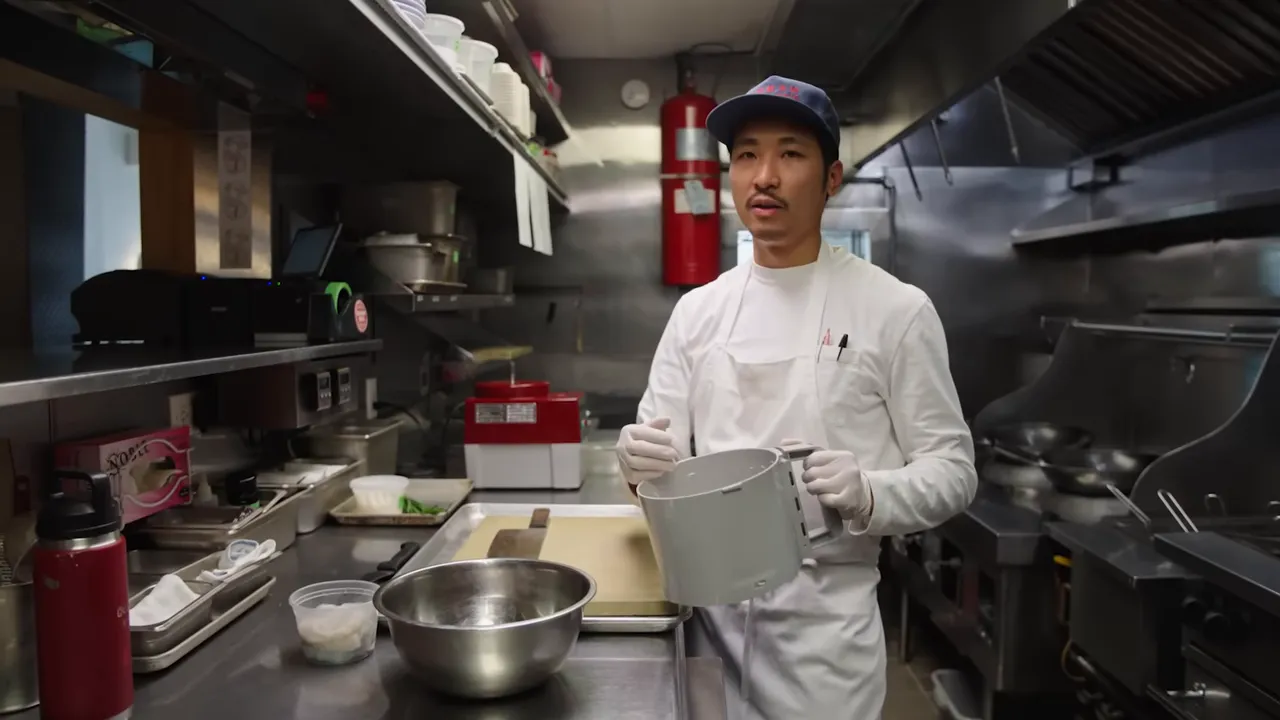 Chef holding a food processor bowl of blended fish and shrimp paste in a professional kitchen