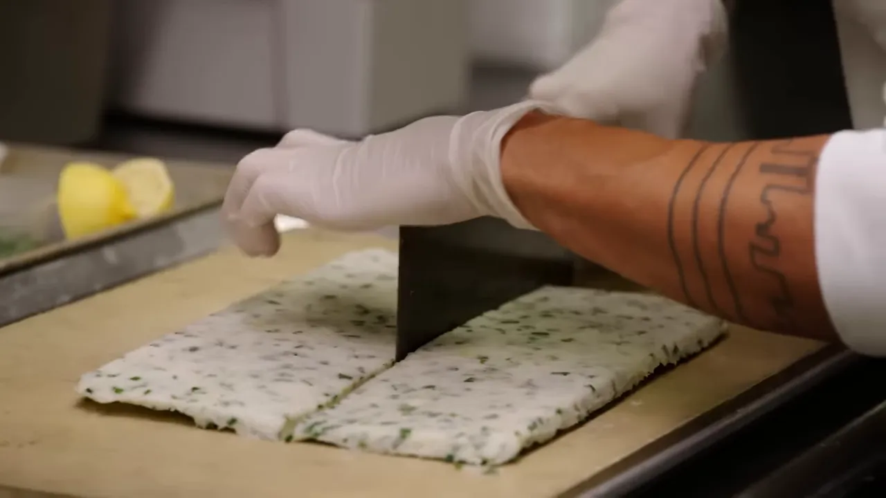 chef cutting a chilled fish-and-shrimp paste slab into rectangular patties with a cleaver