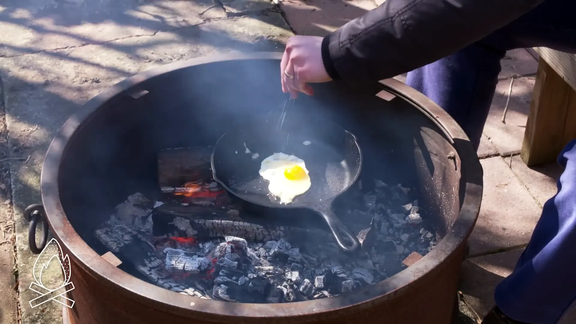 Egg frying in cast iron pan over campfire