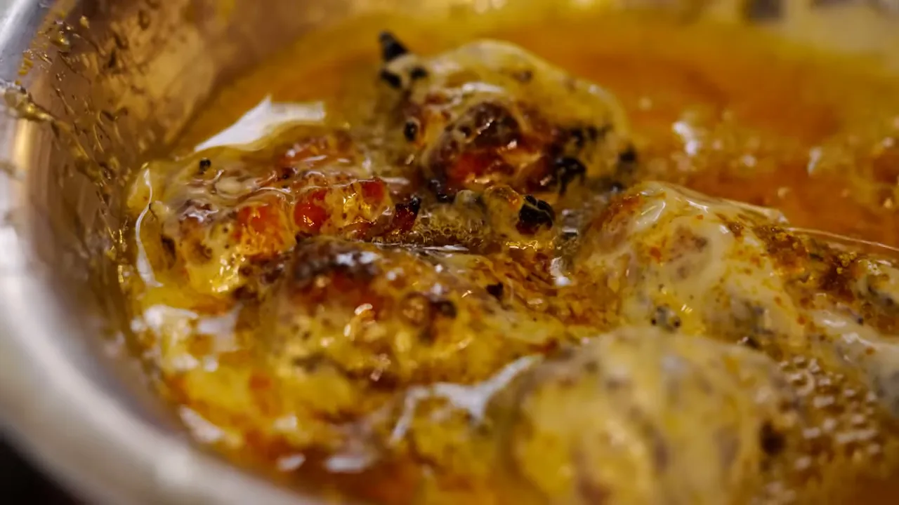 close-up of charred chicken pieces immersed in melted clarified butter and cream in a metal bowl