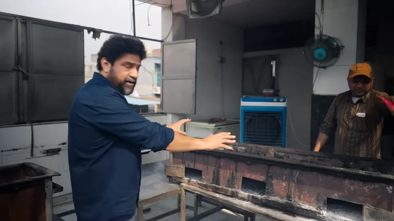 view of long charcoal sigri grills on a rooftop with a cook gesturing and assistant fanning coals