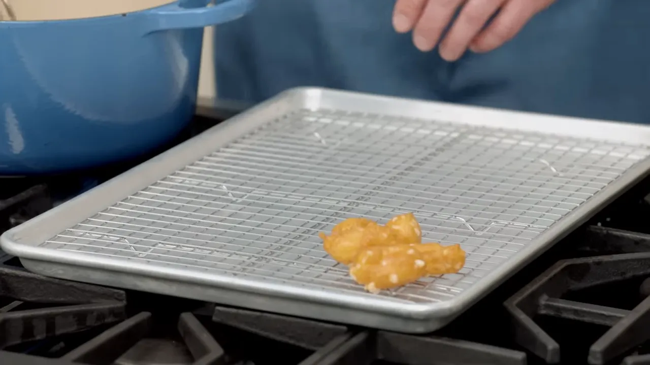 Golden fried cheese curds resting on a wire rack over a baking sheet with a blue pot in the background.