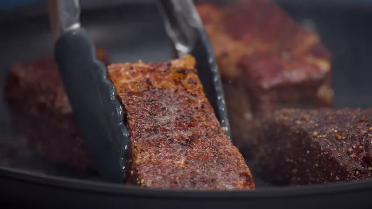 tongs holding a seared short rib showing a dark, crisp crust