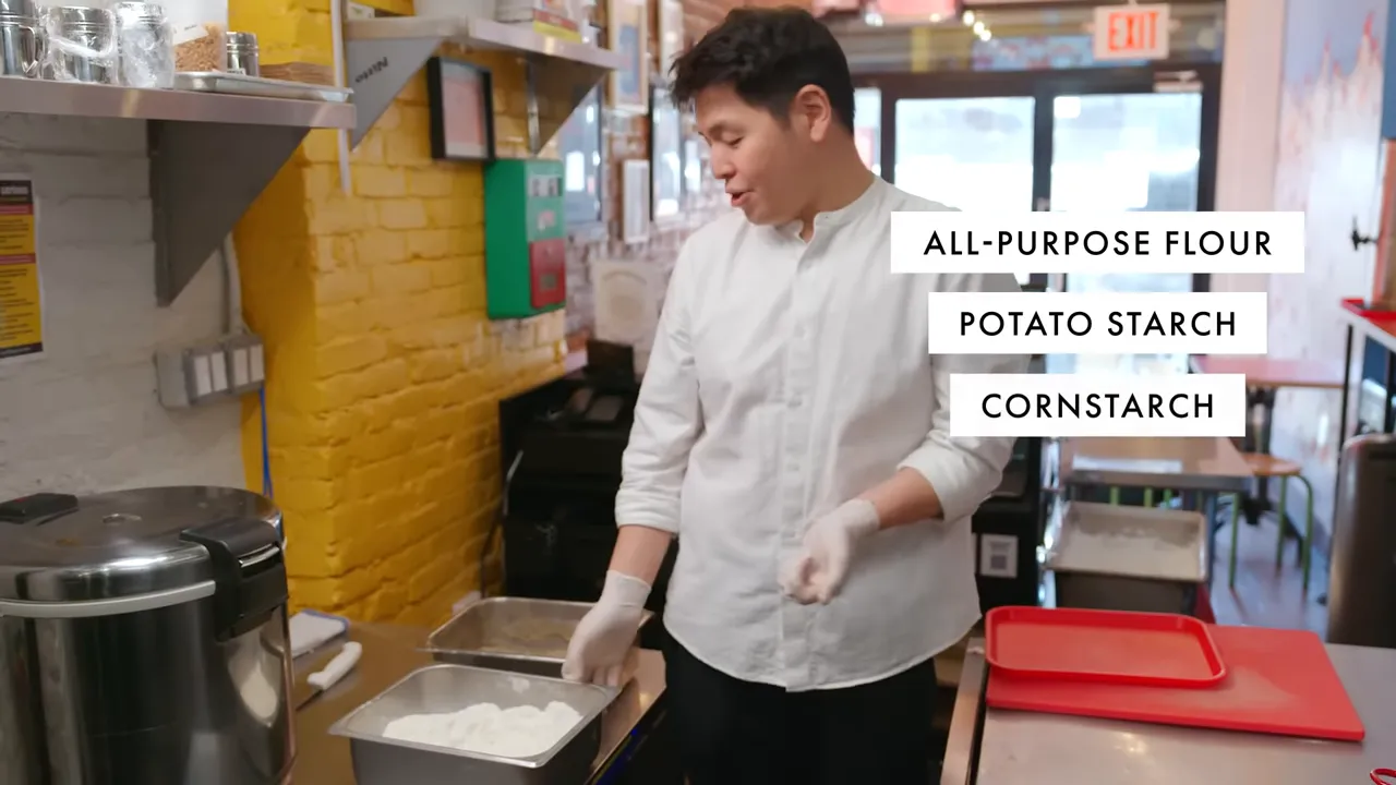 Chef at a prep counter with metal pans of flour and on-screen text listing all-purpose flour, potato starch, cornstarch