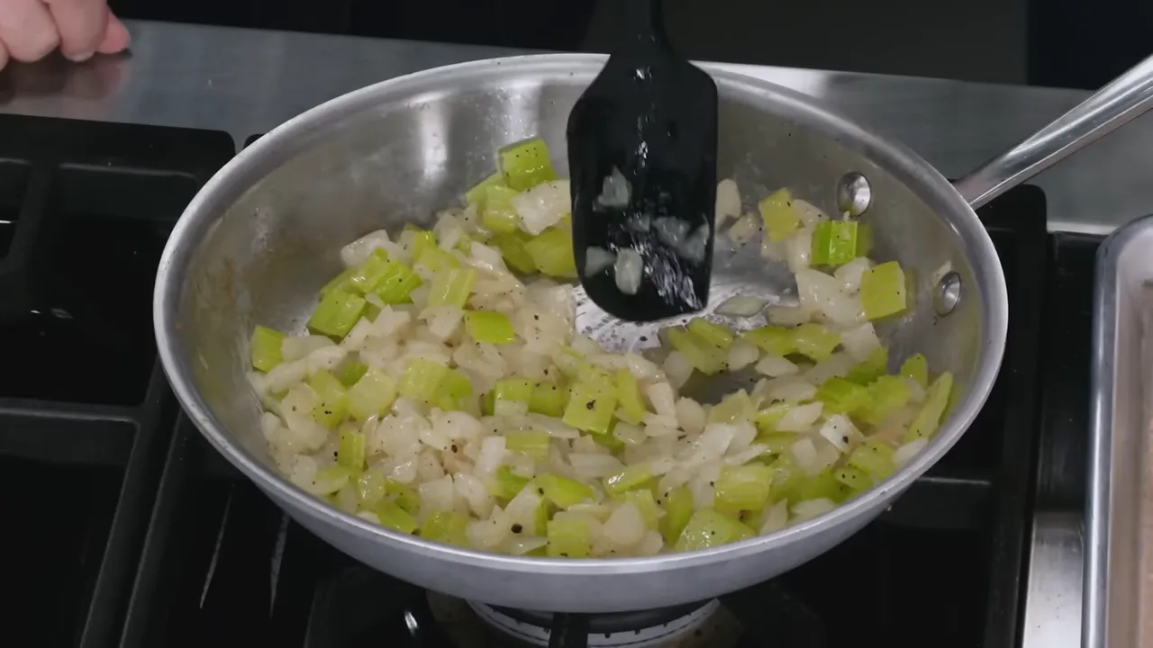 Skillet with sautéed celery and onions being stirred with a spatula.