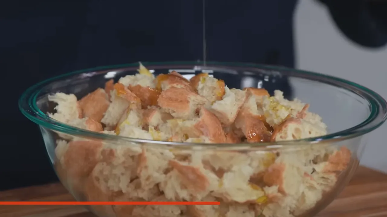 Close-up of torn baguette pieces in a glass bowl with olive oil drizzling onto them.