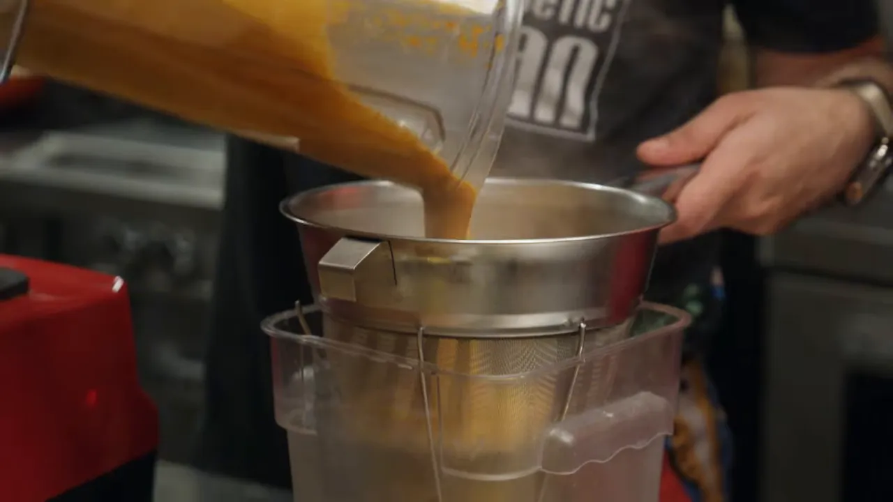 Stream of blended tomato sauce being poured through a fine mesh strainer to create a smooth makhani sauce