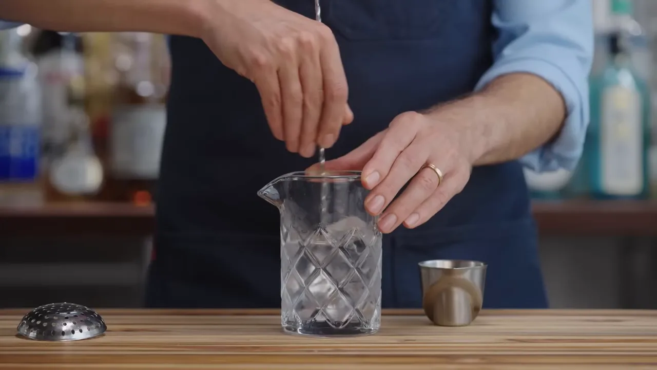 Close up of hand stirring a mixing glass with a bar spoon