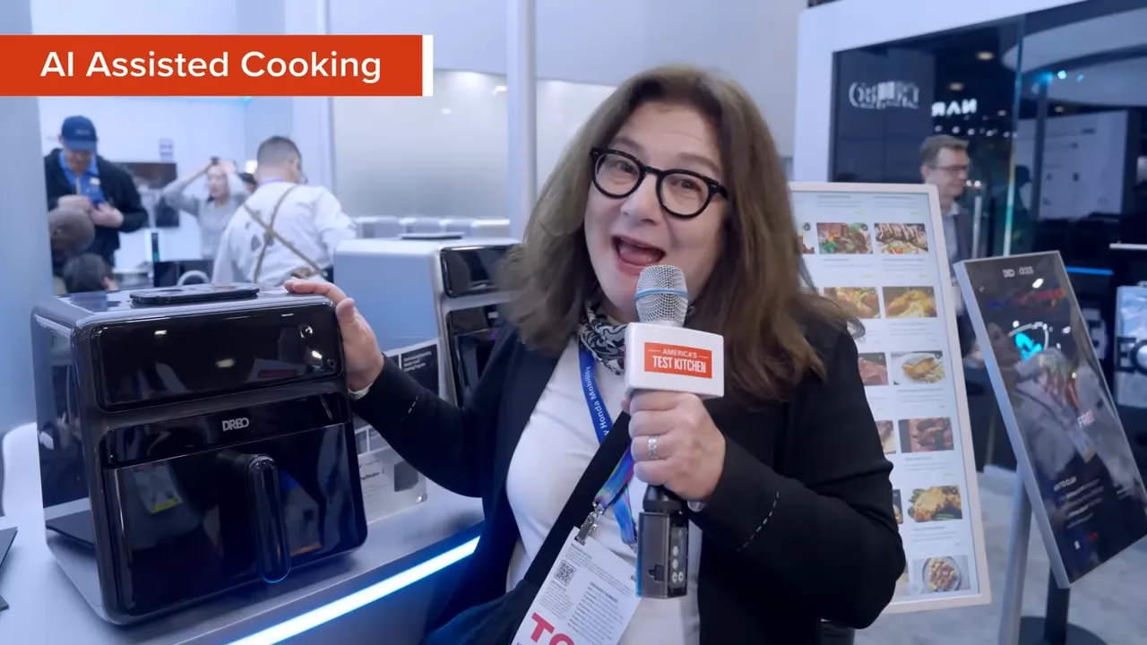 Host demonstrating a black AI-assisted air fryer at a CES booth while holding a microphone