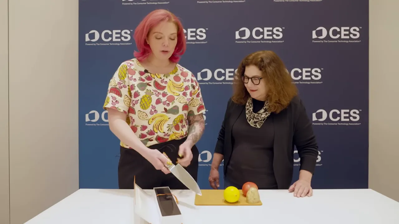 Presenter holding an ultrasonic chef knife over a cutting board with fruit at CES