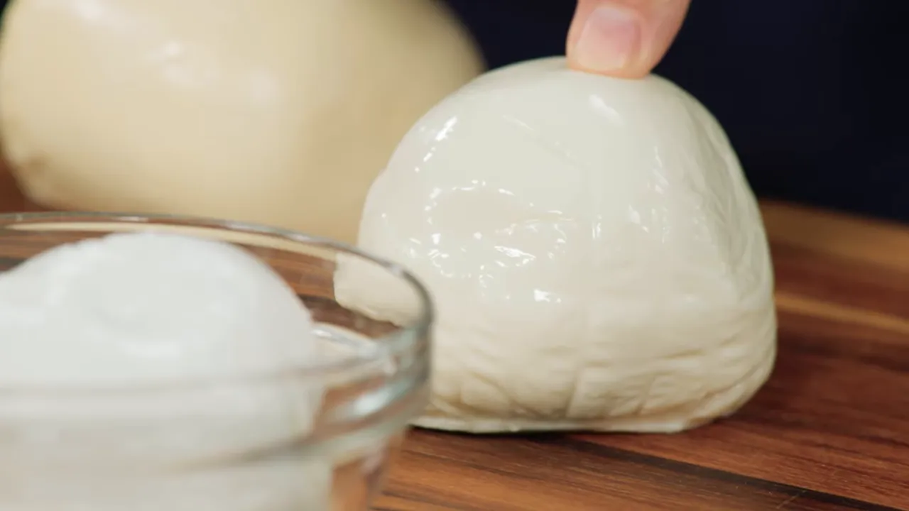 close-up of a fresh mozzarella ball with a finger touching its shiny, moist surface