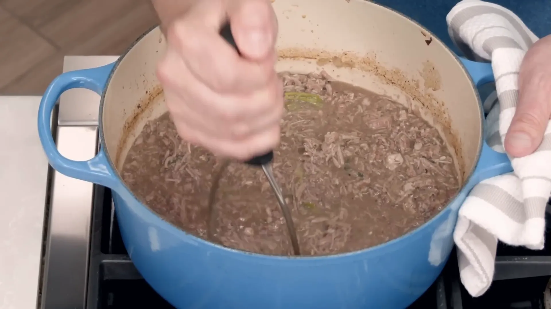 Using a potato masher to shred pork and vegetables