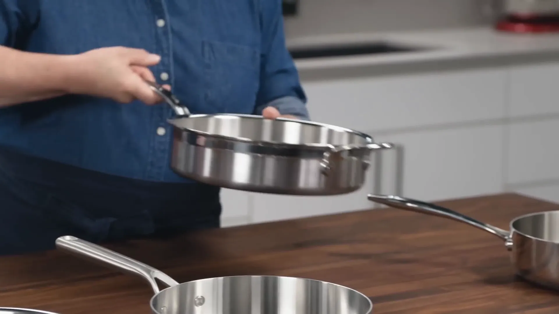 hand picking up sauté pan with curved handle showing uneven weight distribution