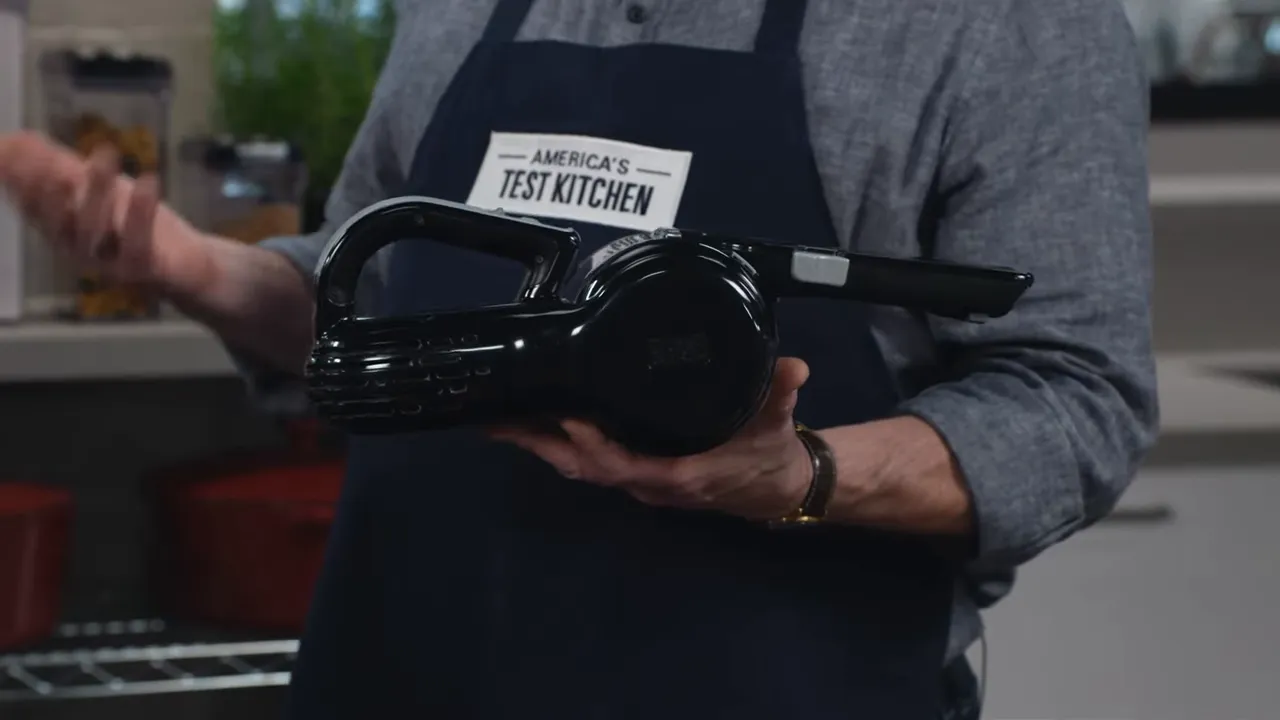 Black & Decker pivot handheld vacuum held in hands against a kitchen test-bench background