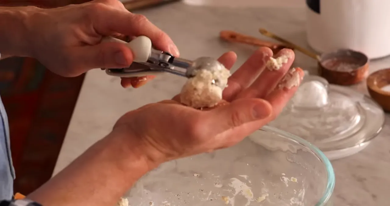 Close-up of hands using a cookie scoop to form a round dough ball over a hand