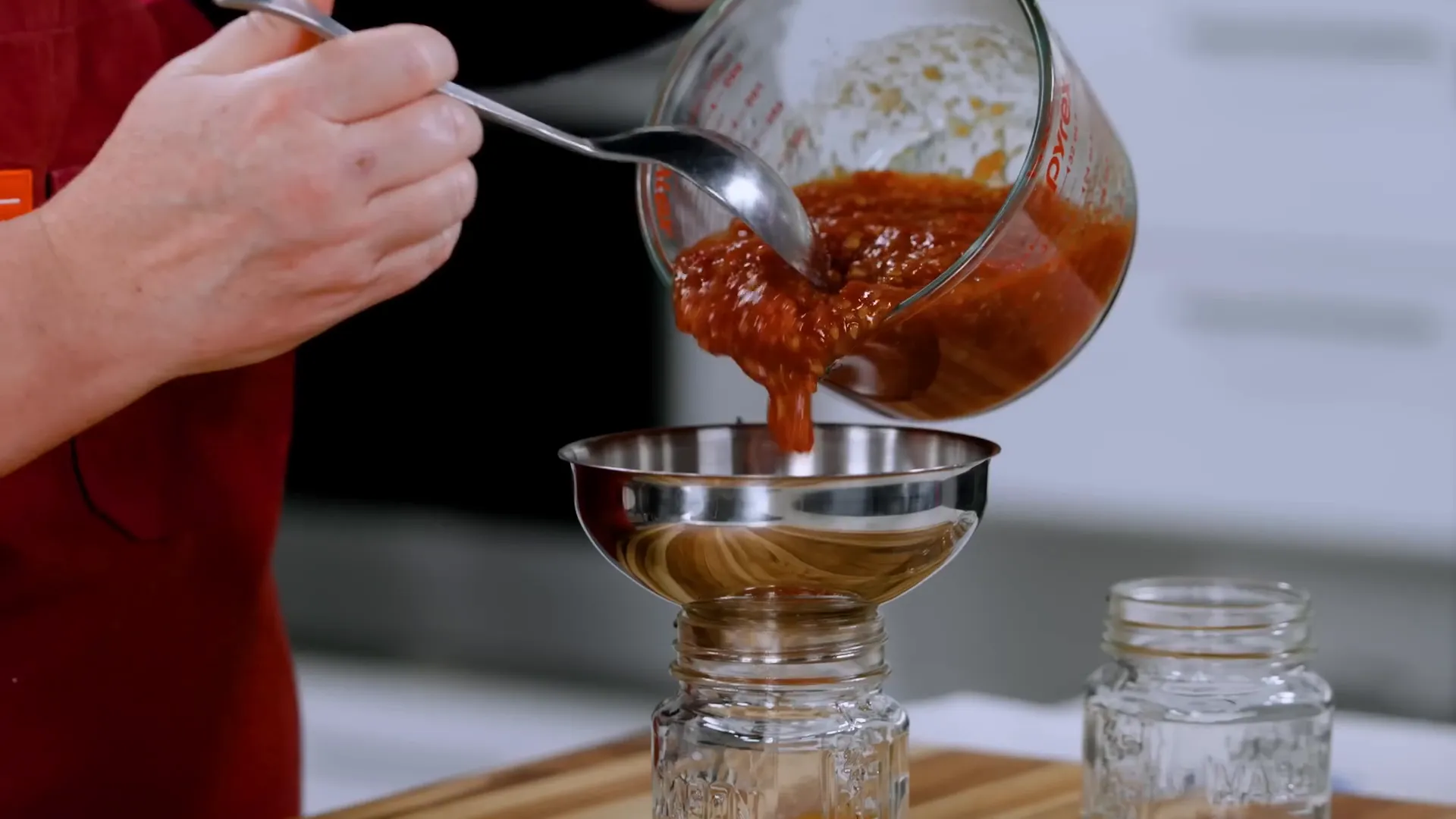 Pouring tomato jam into jars using a funnel