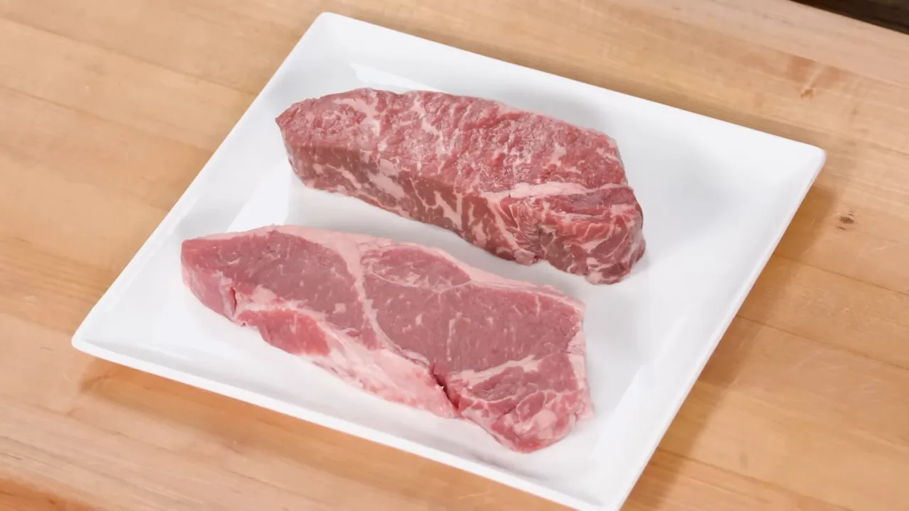 Close-up of two raw steaks on a white plate showing visible marbling and fat
