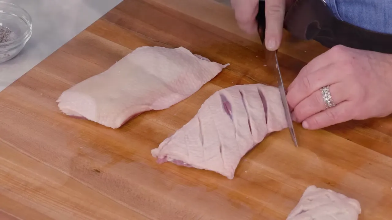 Duck breasts on a cutting board being scored with a knife to create hatch marks in the fat