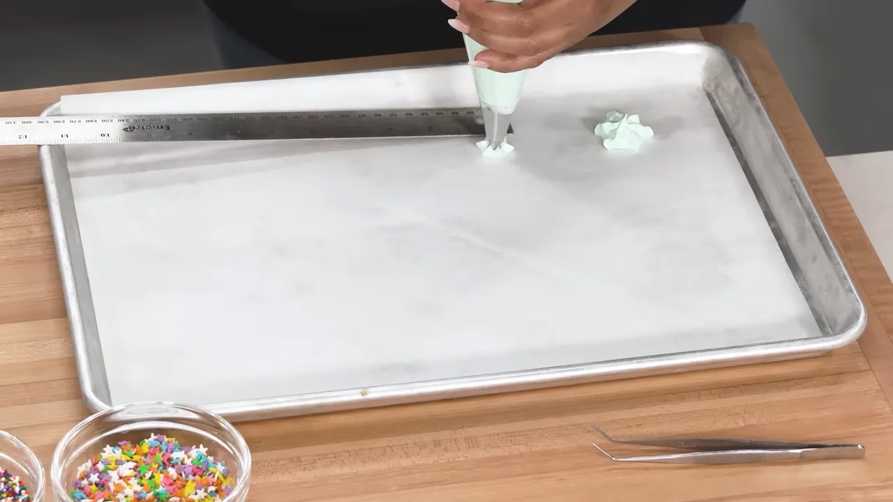 Overhead view of piping small star-shaped meringues onto a parchment-lined tray