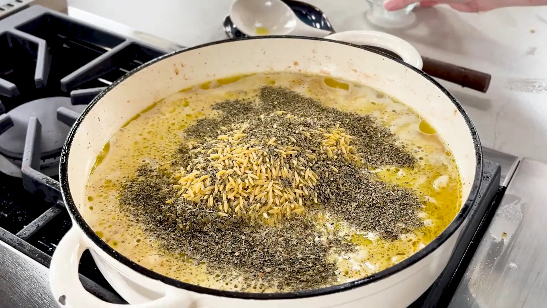 Adding orzo and dried basil to simmering chicken broth