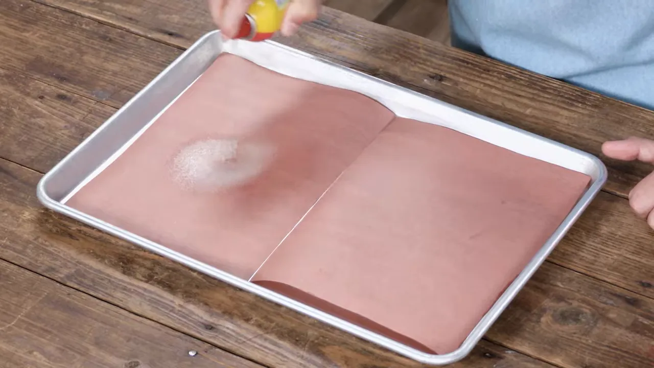 Close-up of a rimmed baking sheet with parchment paper showing a circular spray pattern from a cooking spray can