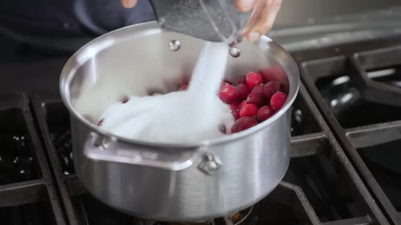 Sugar being poured into a saucepan of frozen cranberries