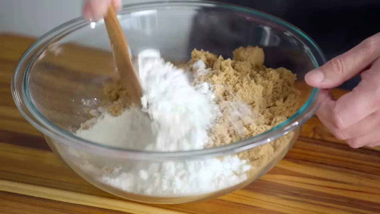 Wooden spoon stirring flour and brown sugar in a large glass mixing bowl