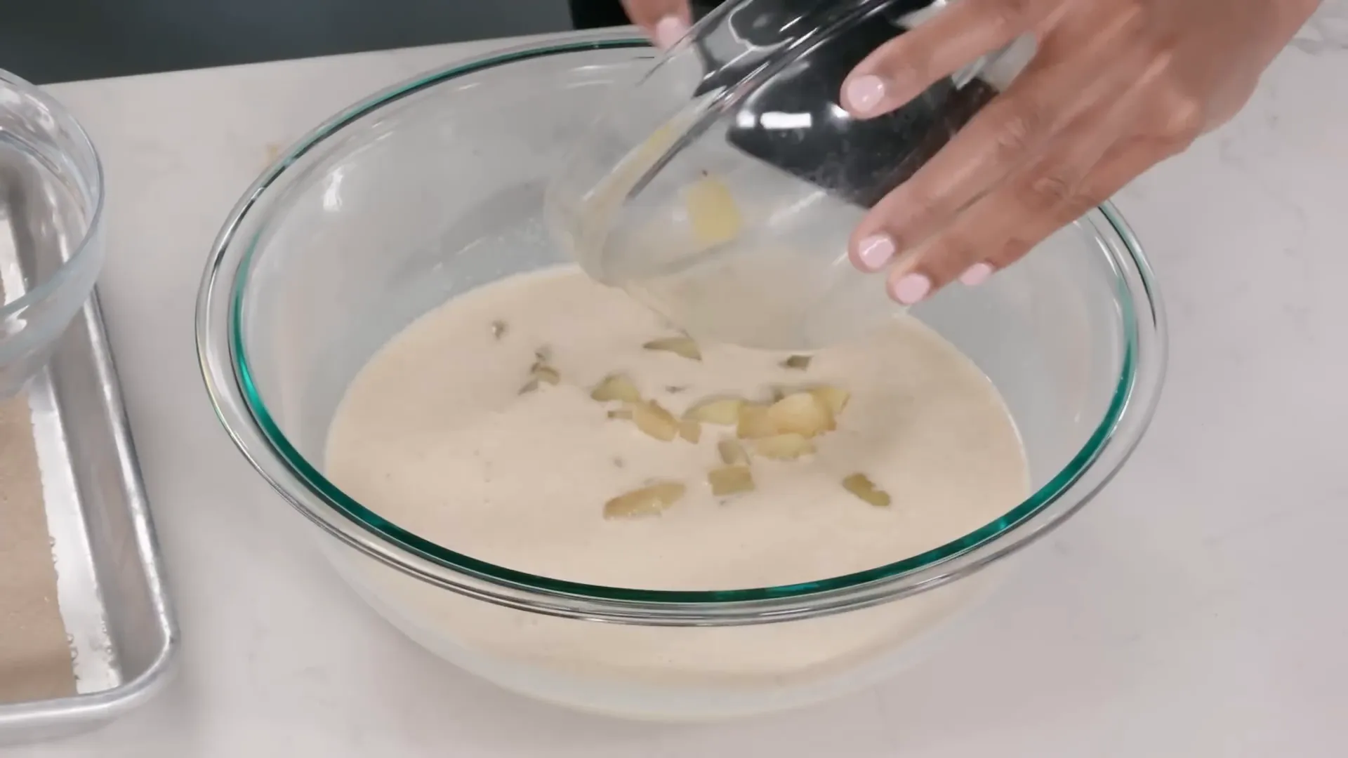 Pouring apple-infused custard over toasted challah cubes in a mixing bowl