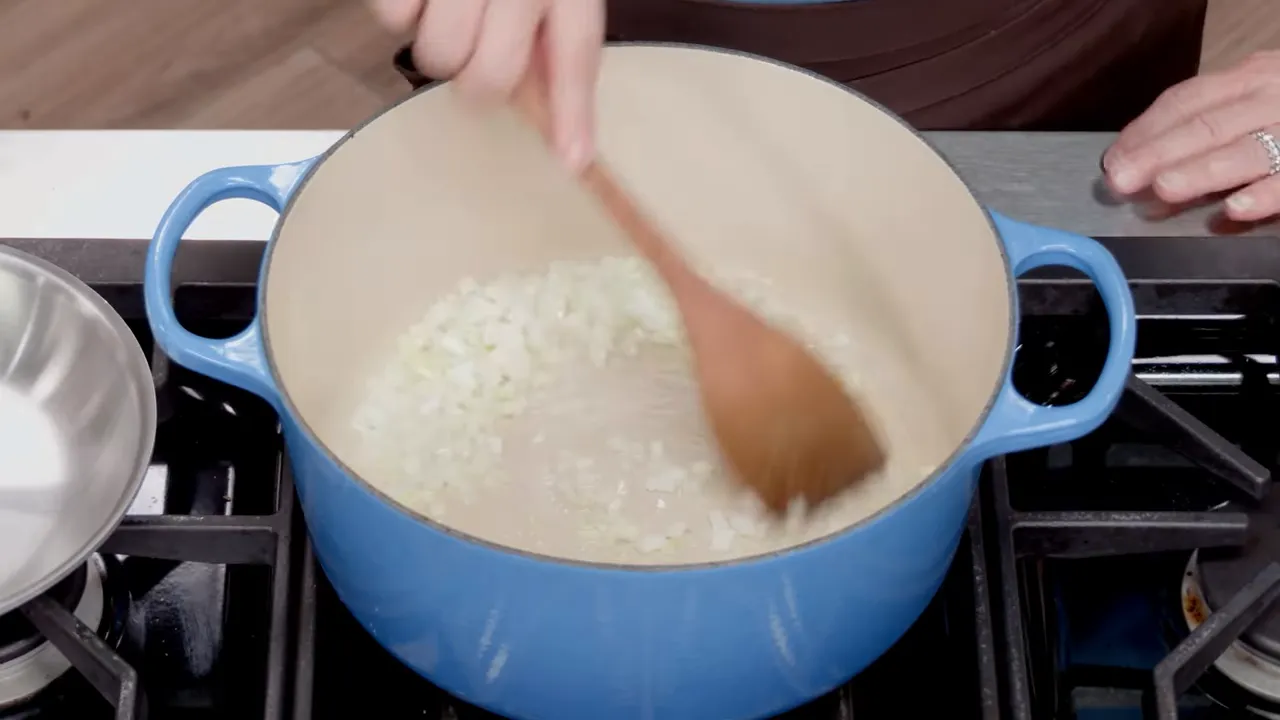 Chopped onions being stirred in a Dutch oven with a wooden spoon