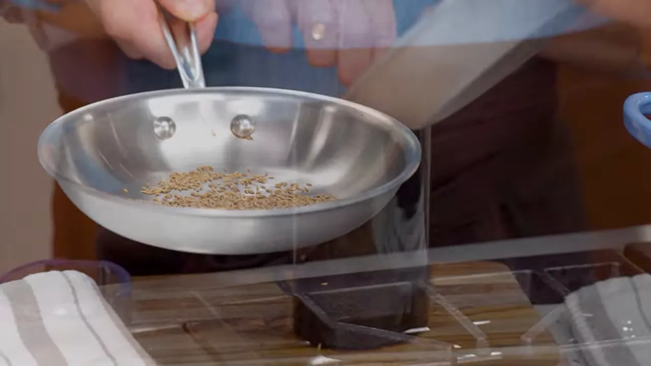 stainless skillet with cumin seeds on stovetop ready to be toasted
