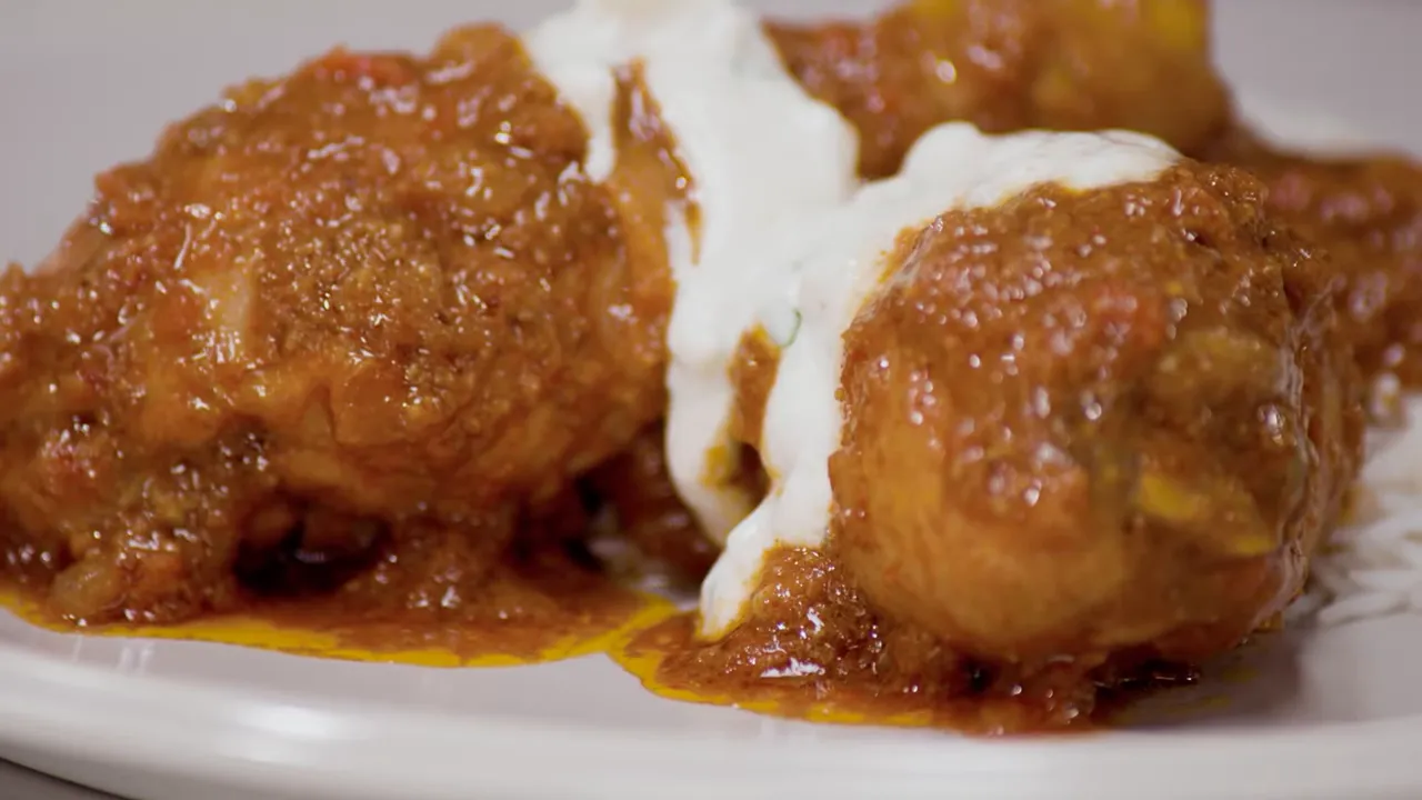 close-up of finished kombdi jira chicken drumsticks with raita drizzled between the pieces and rice on the side