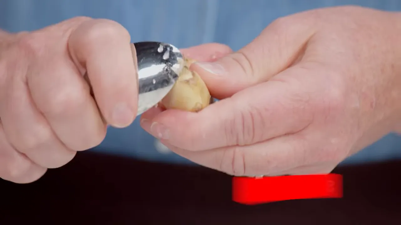 close-up of hands peeling ginger with a spoon for recipe prep