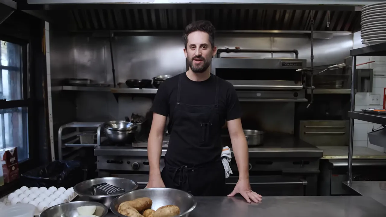Cook standing behind a counter with bowls of Idaho potatoes and a box grater in a restaurant kitchen