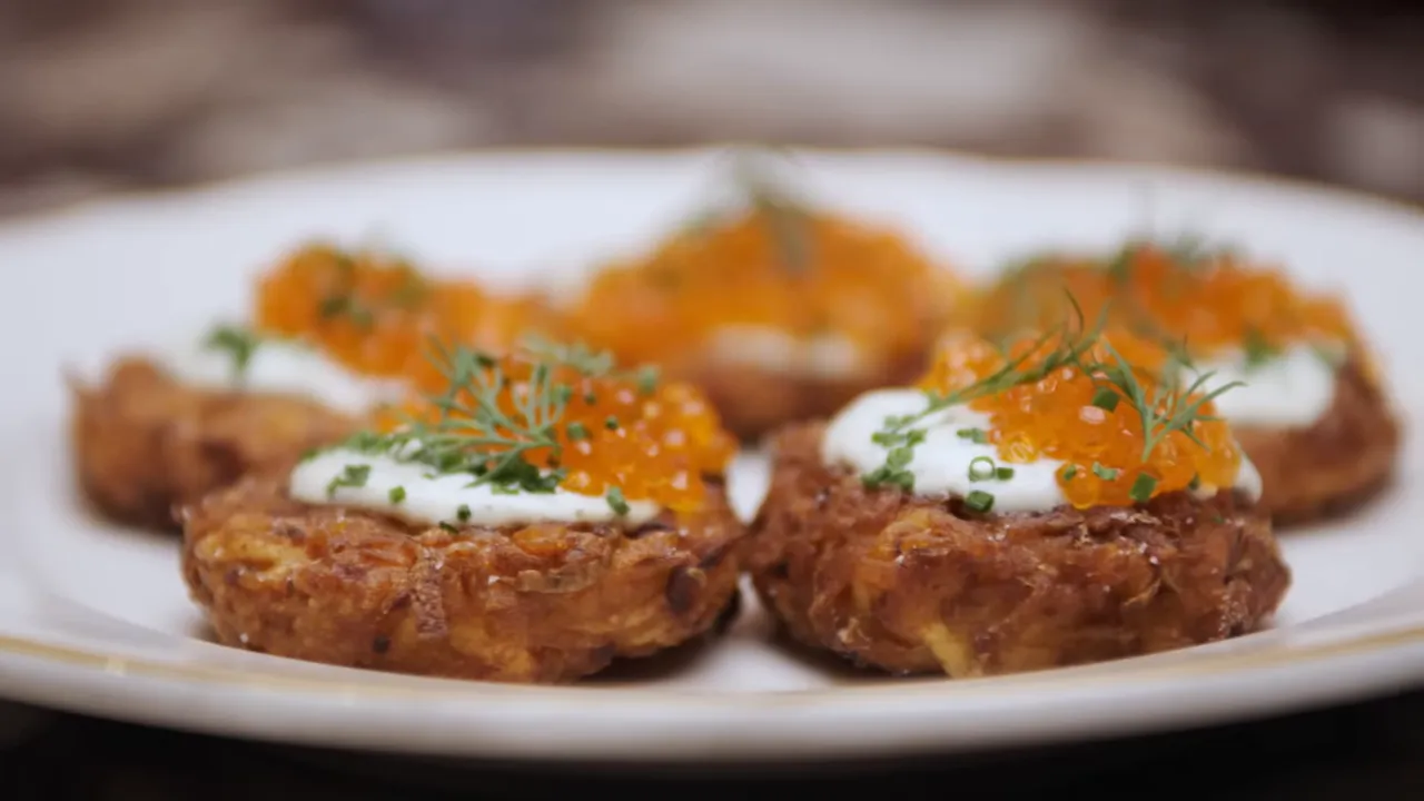 Close-up of golden latkes topped with crème fraîche, orange trout roe and dill