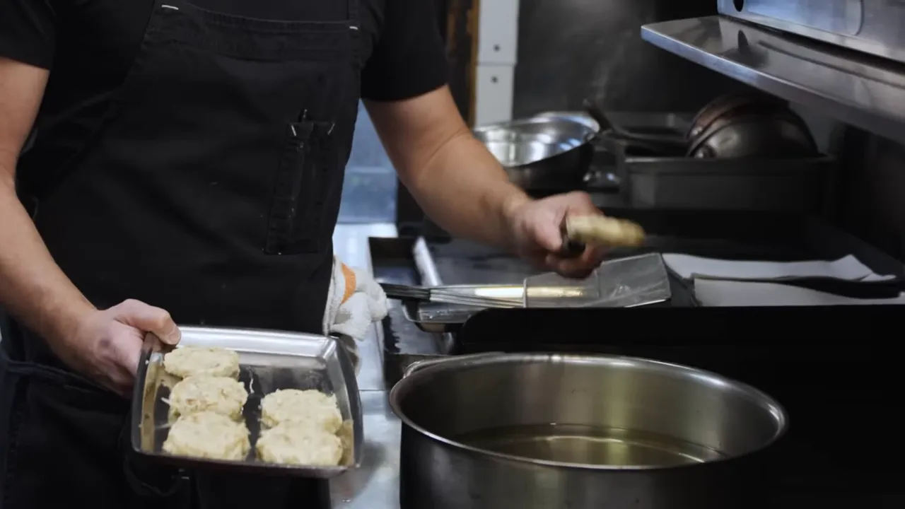 Tray of formed potato latkes being held over a pot of hot frying oil