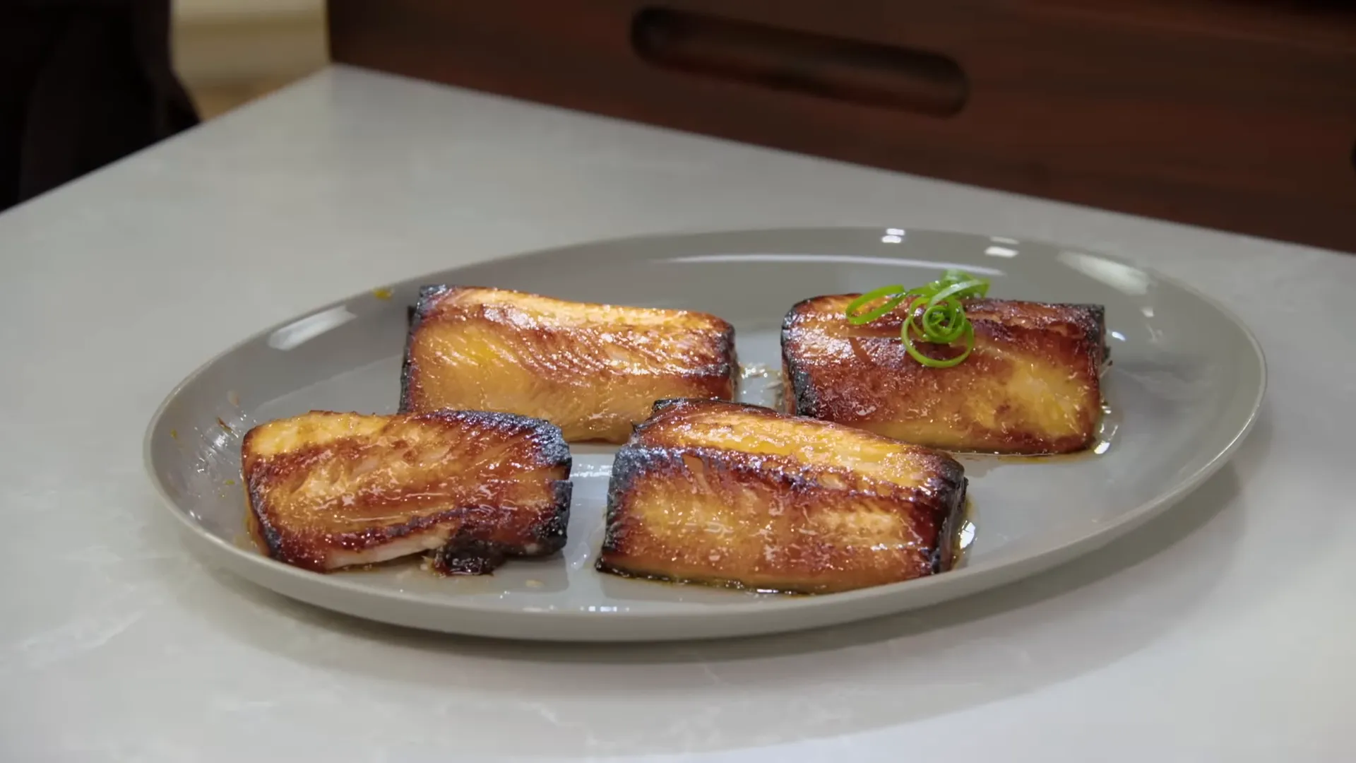 Plated miso black cod with glossy bronze glaze, scallion curls, and pickled ginger