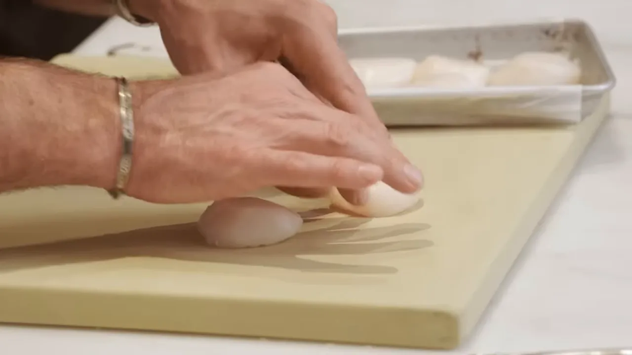 hands arranging scallops on a cutting board with tray of scallops in background