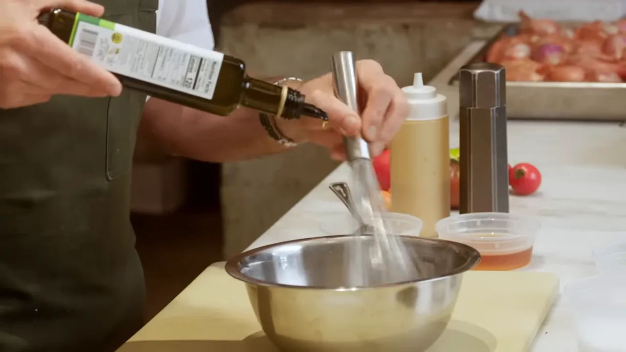 Close-up of olive oil being poured into a mixing bowl while a whisk is in motion