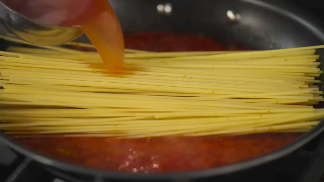 Dropping uncooked spaghetti into a skillet of tomato sauce