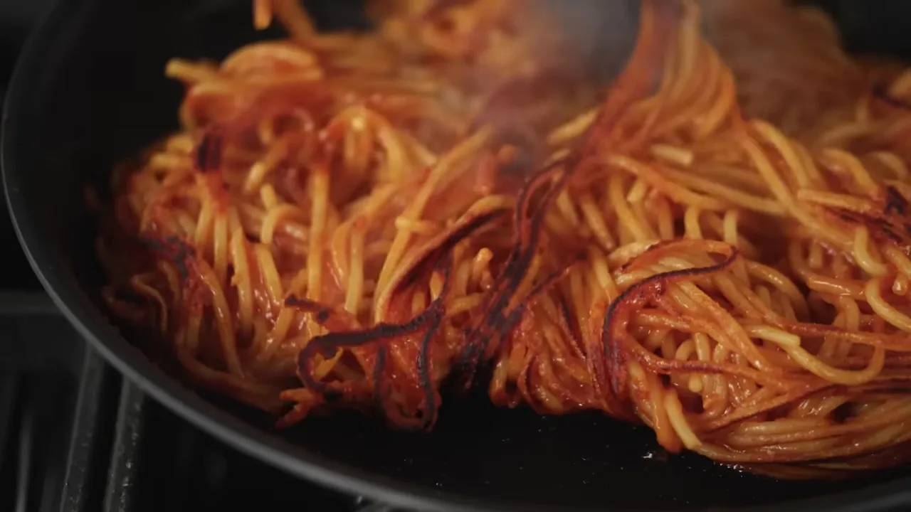 Spaghetti sizzling and beginning to char in the skillet